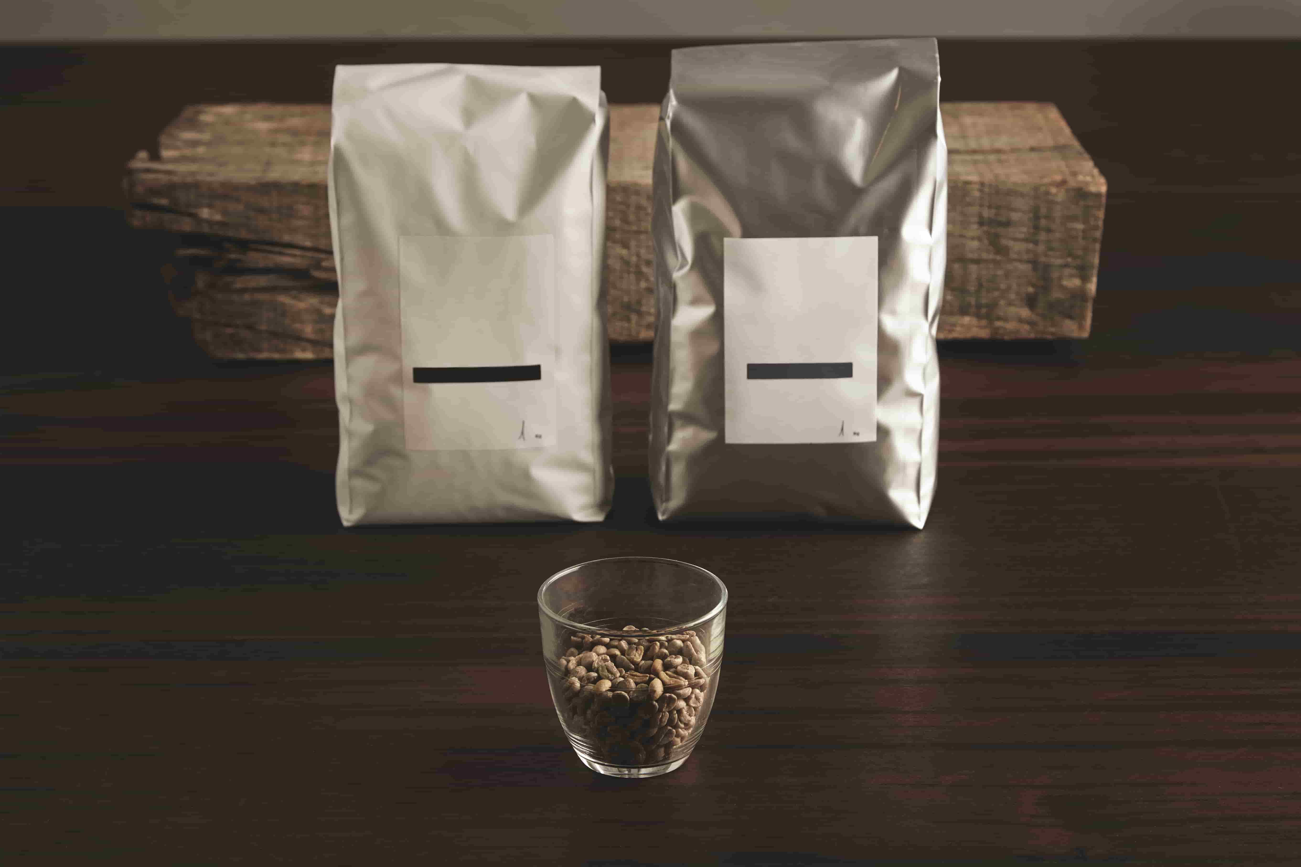 Duas embalagens de plástico flexíveis atrás e xícara com grãos de café
